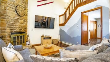 A living room with a stone wall, a fireplace, a flat-screen TV, a wooden staircase, and a mountain mural.