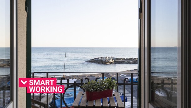 Un balcon avec vue sur la mer, un pot de fleurs rouge orné de plantes et une pancarte indiquant « ESPACE DE TRAVAIL INTELLIGENT ».
