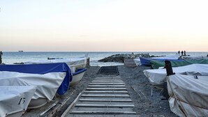 Une plage où se trouvent des bateaux à l’abri et une promenade en bois qui mène à l’eau.