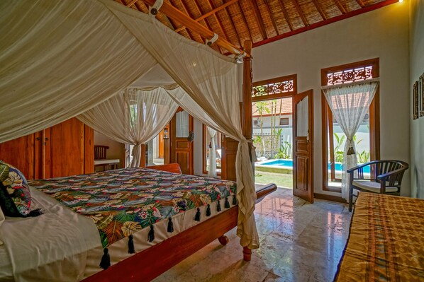 A room with a bed, a table, and a chair. There is a window with a view of the outside.
