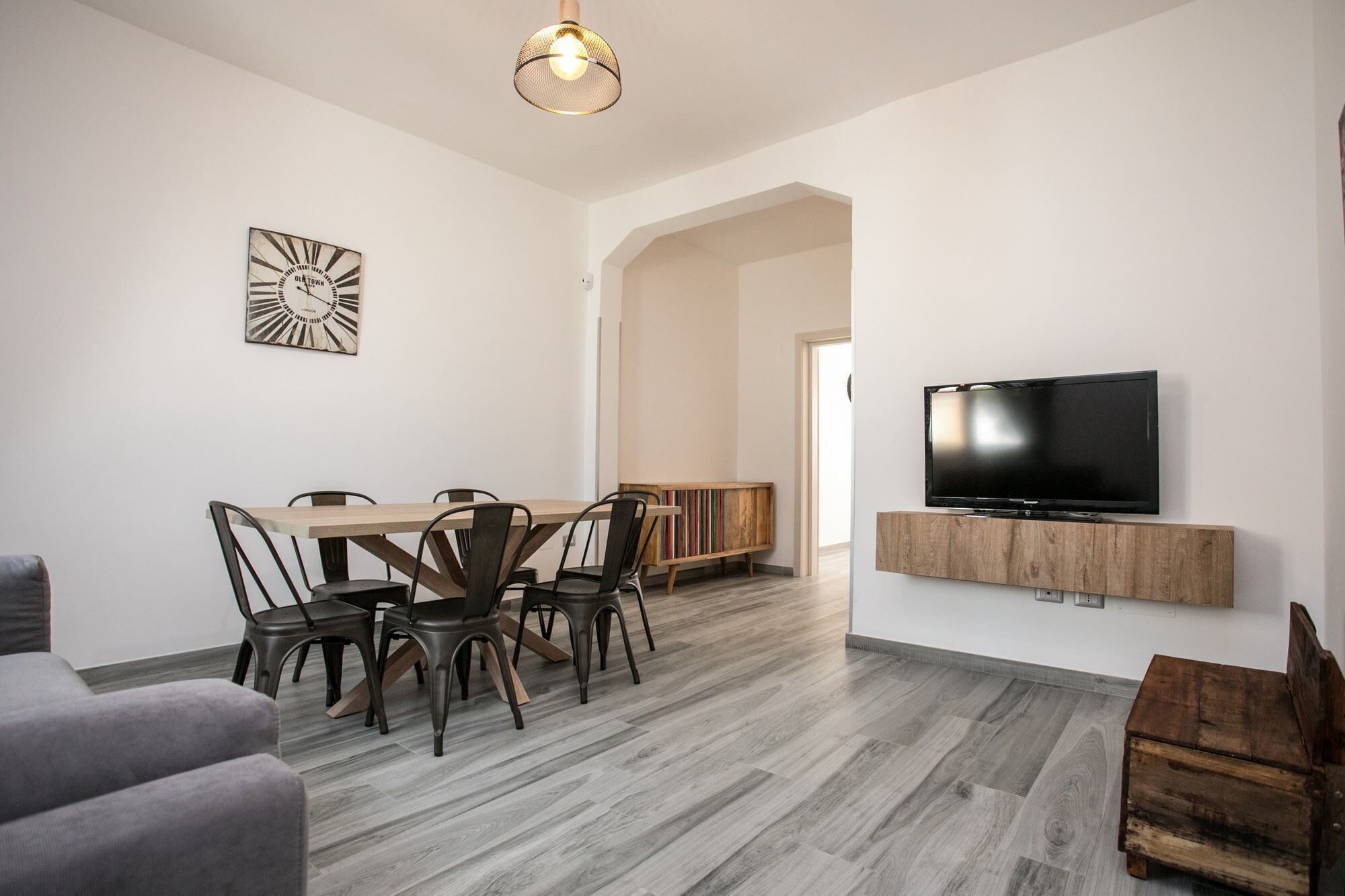 Een moderne woonkamer met een eethoek, een flatscreen televisie bevestigd aan een houten plank en een grote klok aan de muur.