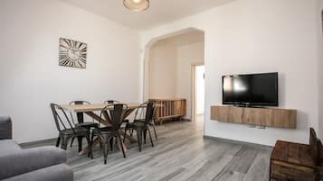 Een moderne woonkamer met een eethoek, een flatscreen televisie bevestigd aan een houten plank en een grote klok aan de muur.