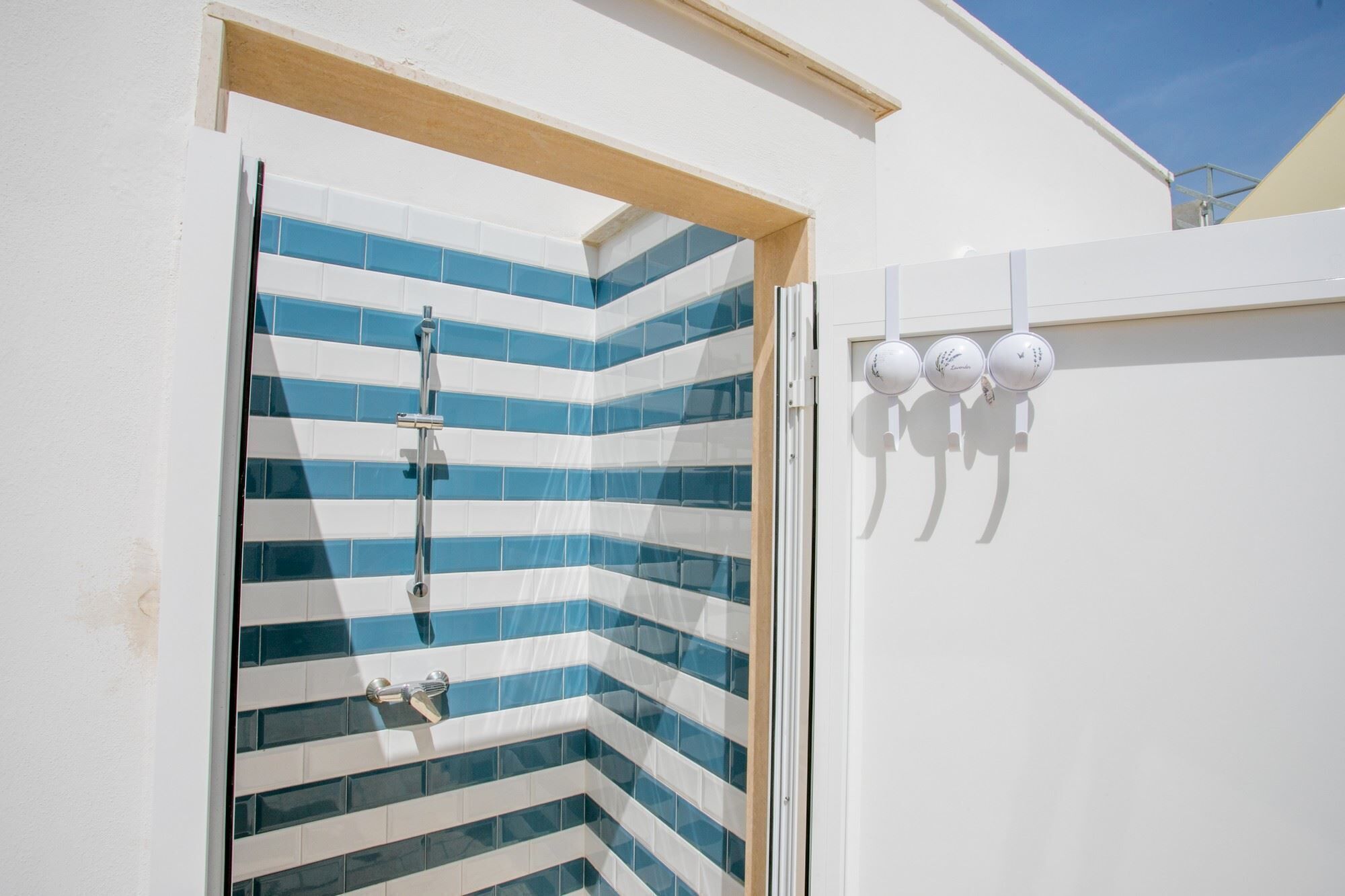 Eine Dusche mit blauen und weißen Fliesen, einem Holzrahmen und einer weißen Wand mit drei runden Leuchten.