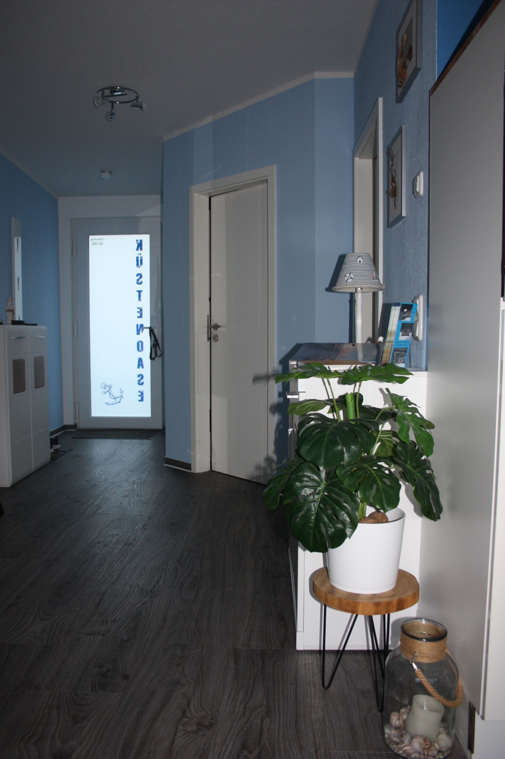 A hallway with a potted plant, a lamp, and a glass jar on a small table.