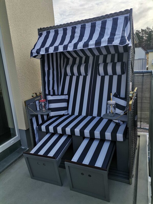 Un espace extérieur aménagé avec des sièges à rayures noires et blanches, comprenant une petite table et des chaises, une bouteille et une tasse.