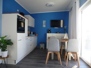Une cuisine compacte avec des meubles blancs, un four à micro-ondes et une machine à café. On y trouve également un coin repas avec une table en bois et des chaises grises.