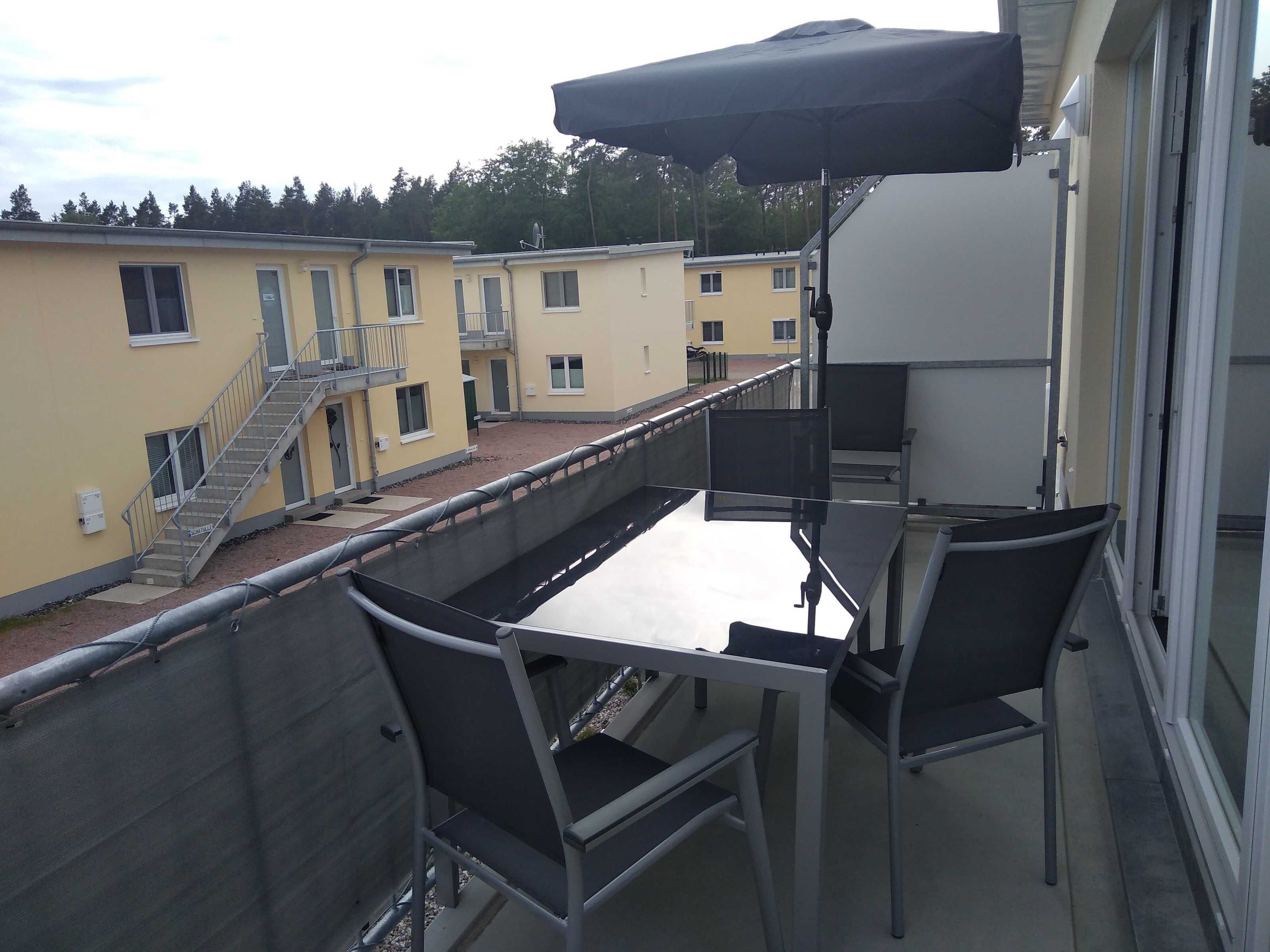 Ein Balkon mit Tisch und Stühlen, einem schwarzen Sonnenschirm und Blick auf angrenzende Gebäude.