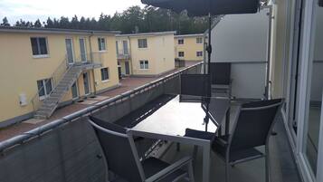 Ein Balkon mit Tisch und Stühlen, einem schwarzen Sonnenschirm und Blick auf angrenzende Gebäude.