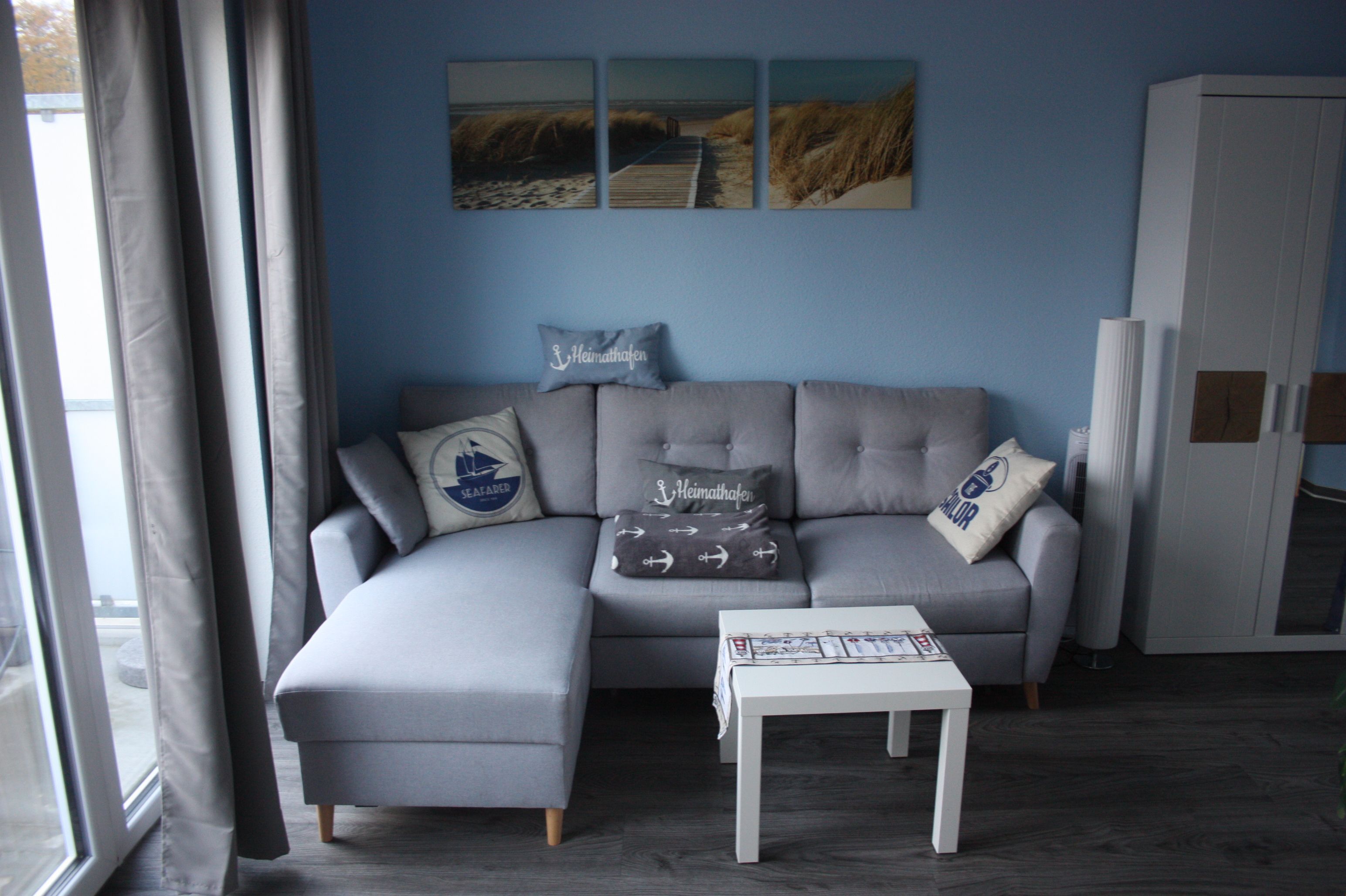 En moderne stue med en grå hjørnesofa, et lille hvidt bord og et hvidt skab.