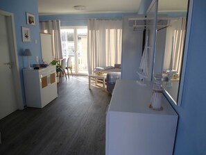 A room with a bed, a desk, a chair, a small table with a plant, and a window with curtains.