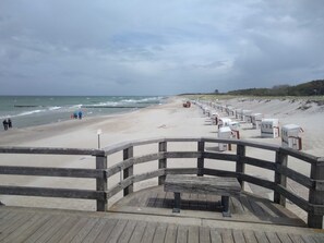 Une promenade en bois menant à une plage où se trouvent des cabanes de plage numérotées.