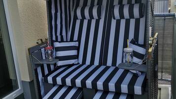 Een zwart-wit gestreept zitgedeelte buiten, met een kleine tafel, stoelen, een fles en een kop.
