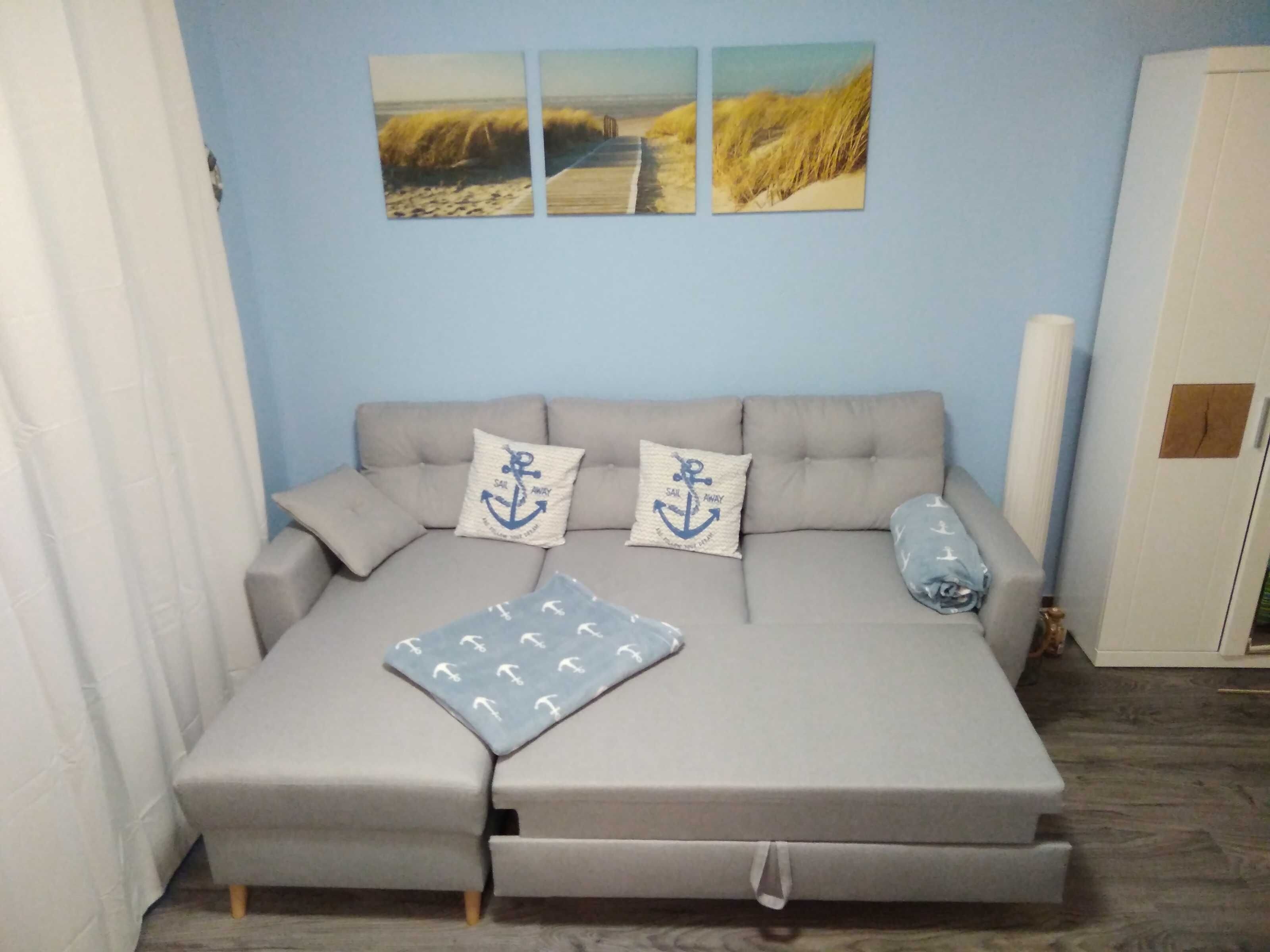 Ein Schlafsofa mit Kissen und Decke, sowie eine Wand mit drei Landschaftsbildern.