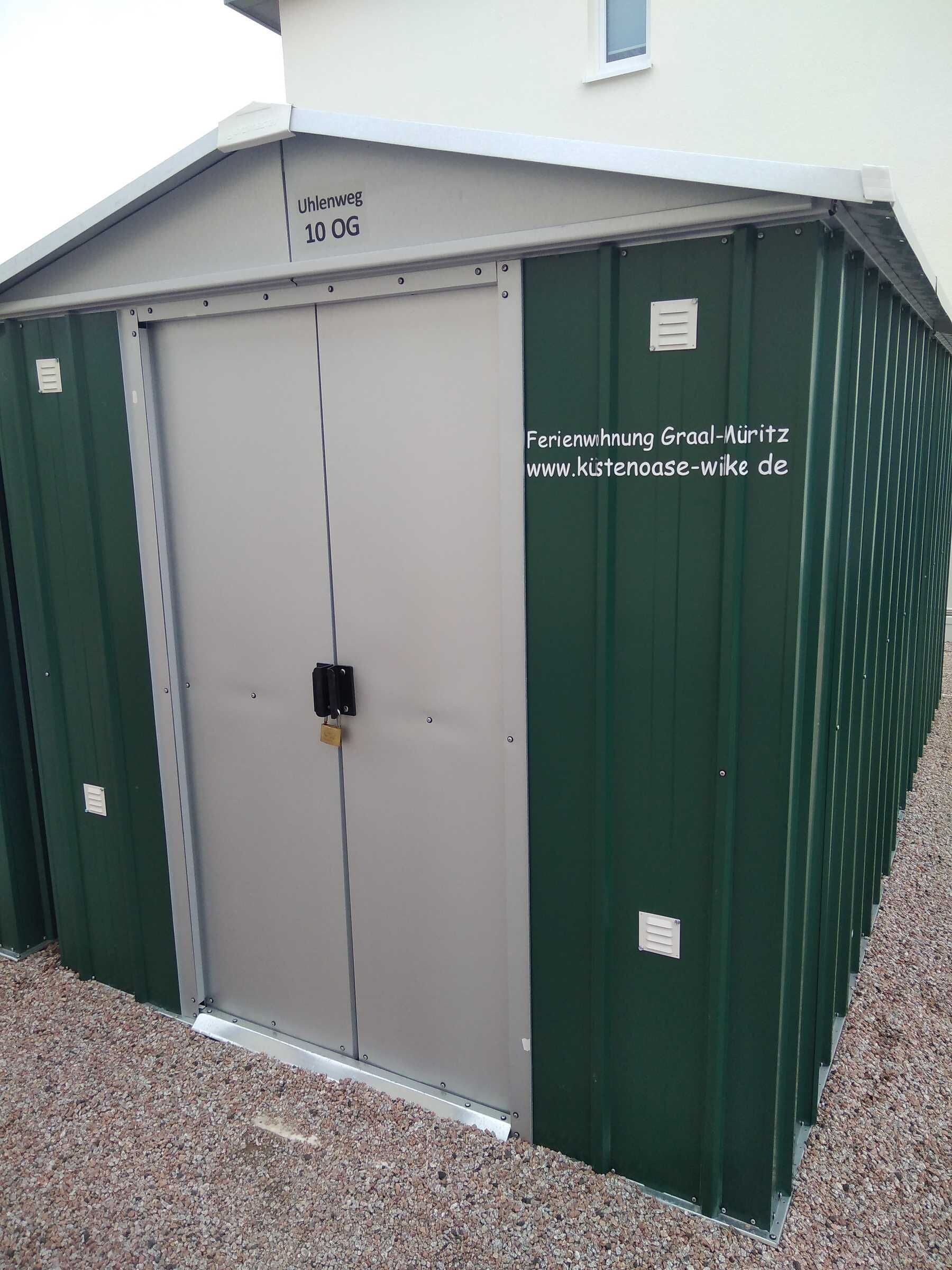 Eine grüne Metallhütte mit einer grauen Tür, mit der Aufschrift 'Uhlenweg 10 OG'.