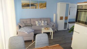 A living room with a sofa, two armchairs, a small table, and a kitchen area with a refrigerator.