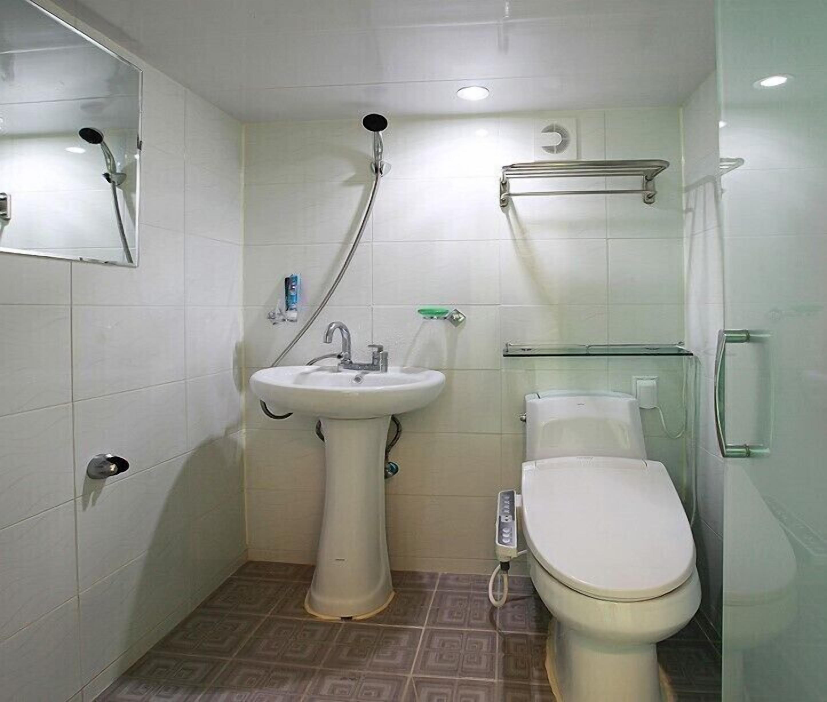 Un baño pequeño y moderno con lavamanos pedestal, inodoro y ducha.