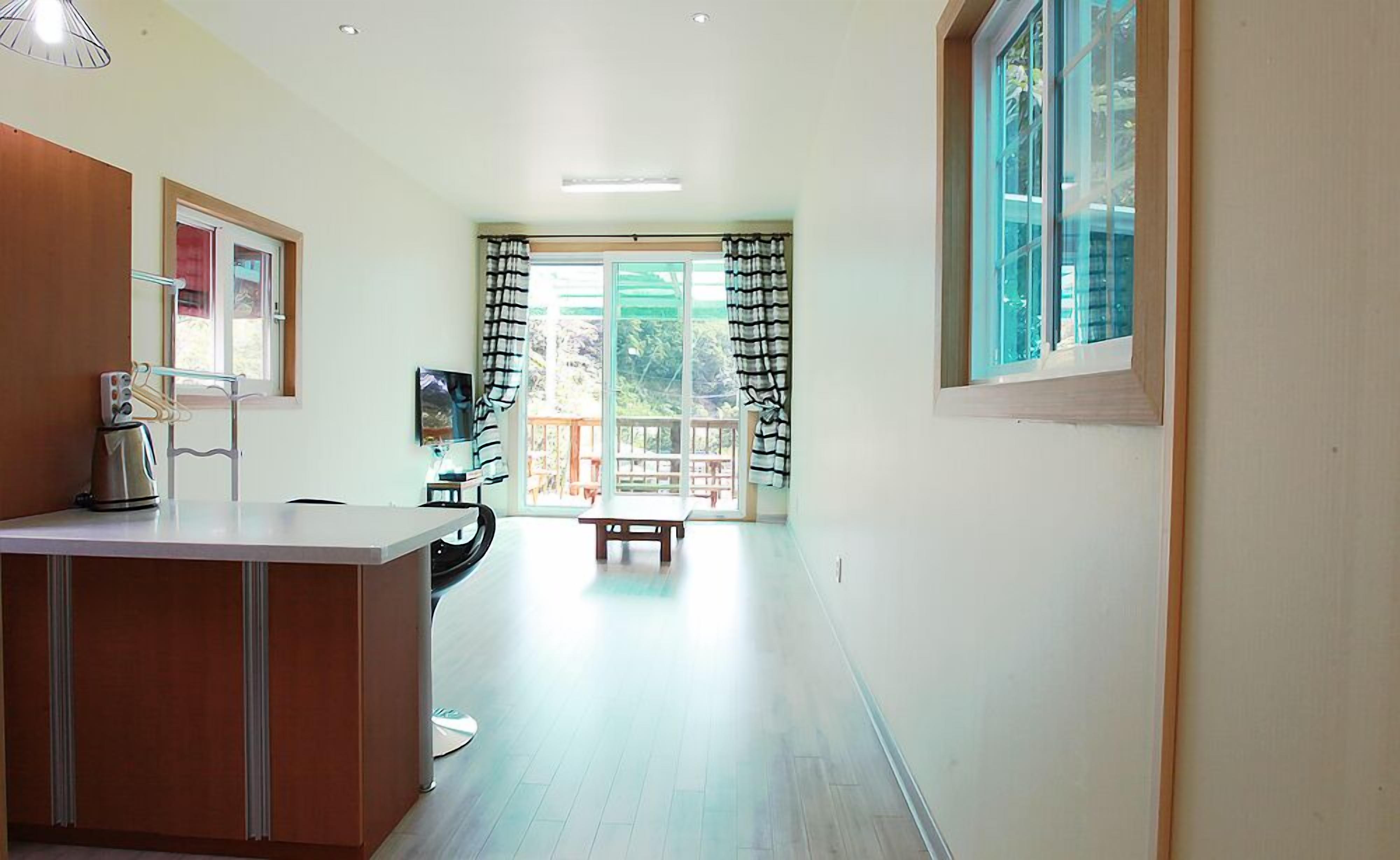 A bright, spacious hallway with a kitchen area on the left, a dining table in the center, and a large window on the right.