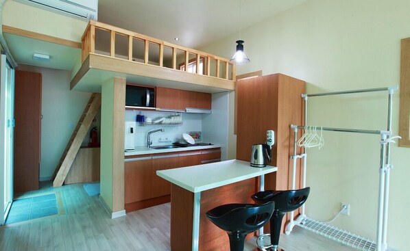 A compact kitchen with wooden cabinets, a microwave, a kettle, and a small dining area with two chairs.