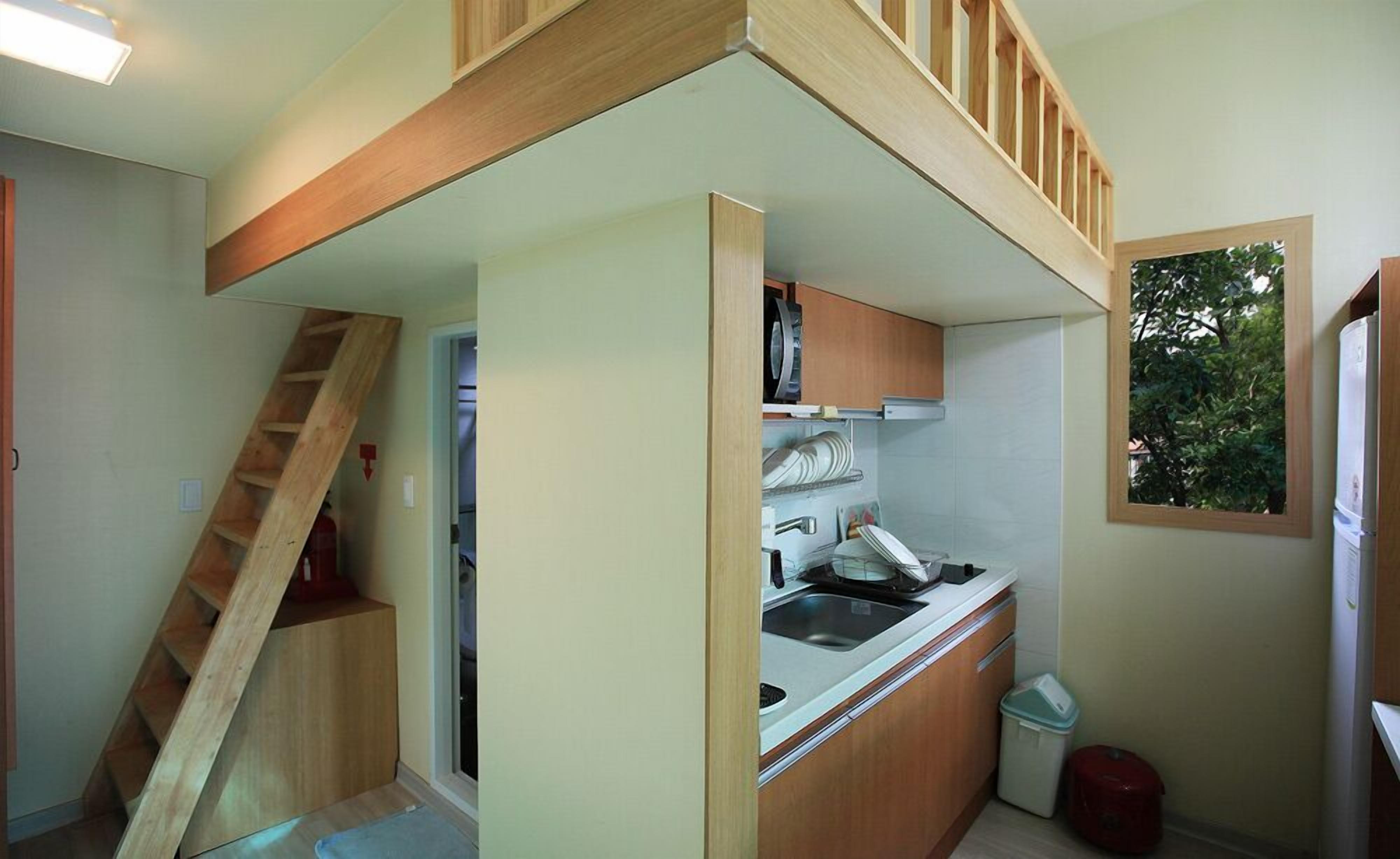 A compact kitchen with a built-in stove, wooden cabinets, and a small trash bin.