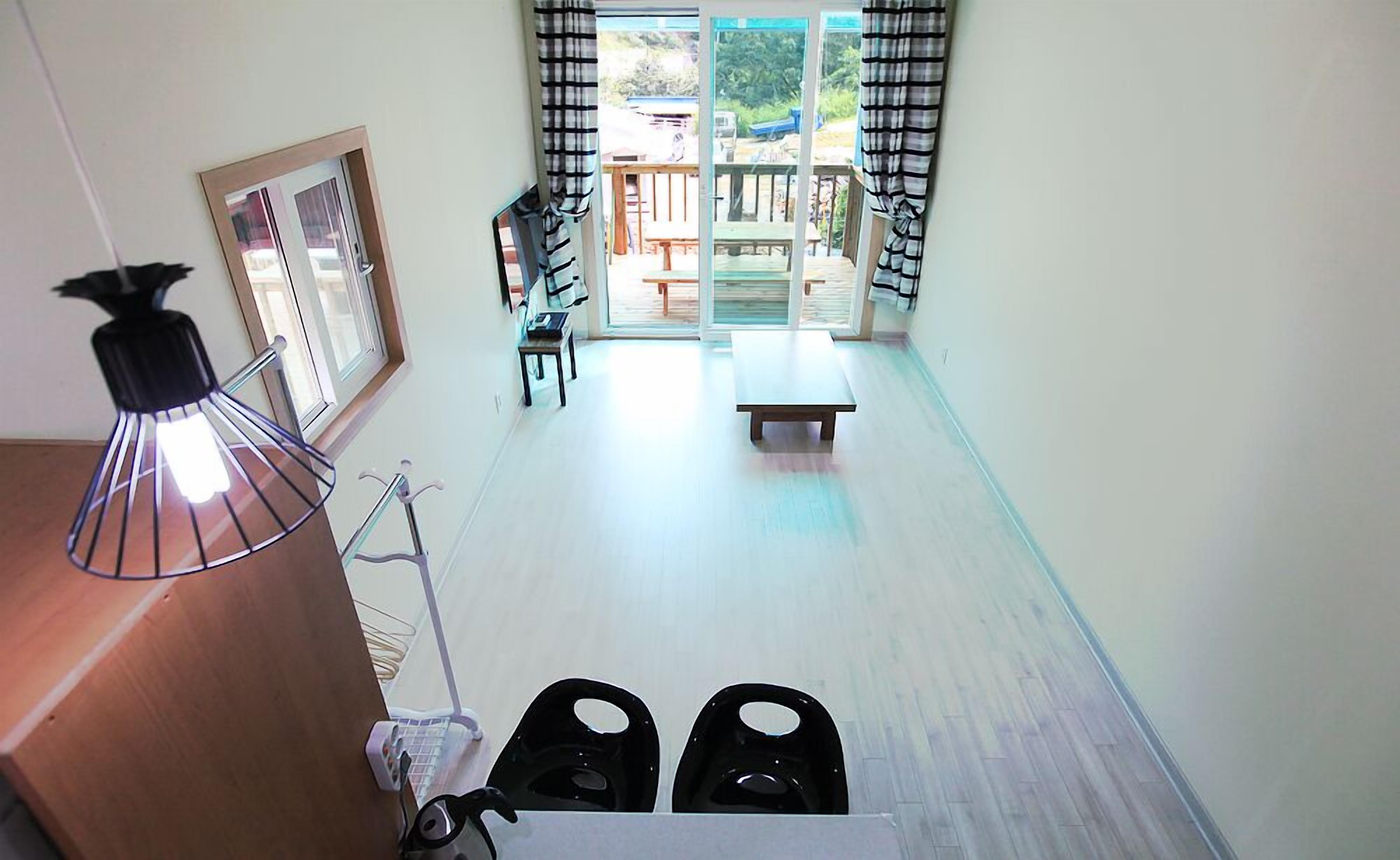 A room with a wooden floor, a bench, a table, and a view of an outdoor patio area with a table and chairs.