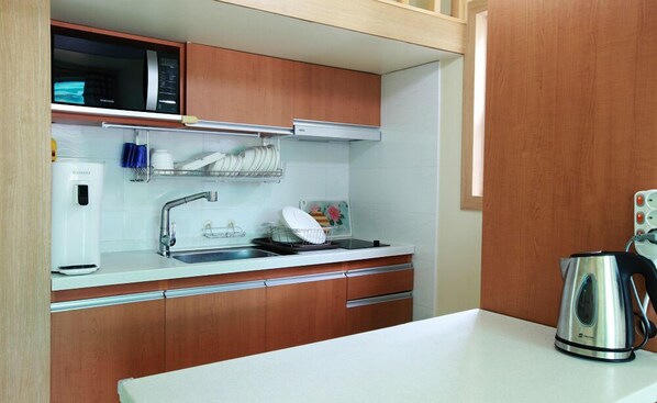 A kitchen with wooden cabinets, a stainless steel sink, a microwave, and a kettle.