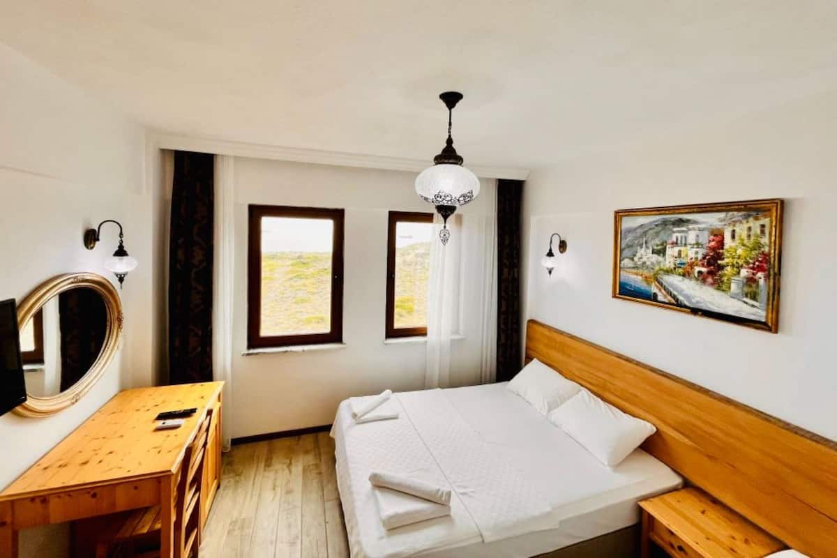 A hotel room with a bed, wooden desk, and a painting on the wall.