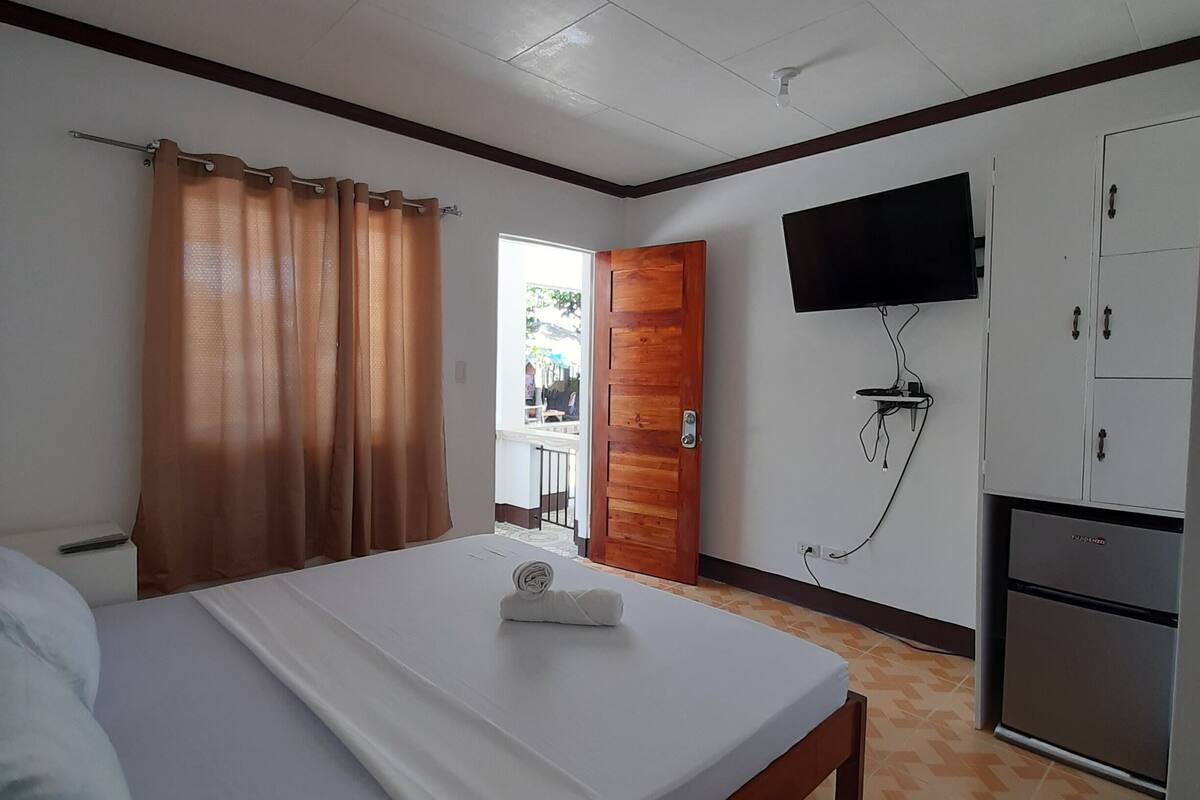 A hotel room with a bed, a television mounted on the wall, a wardrobe, and a door leading to a balcony.