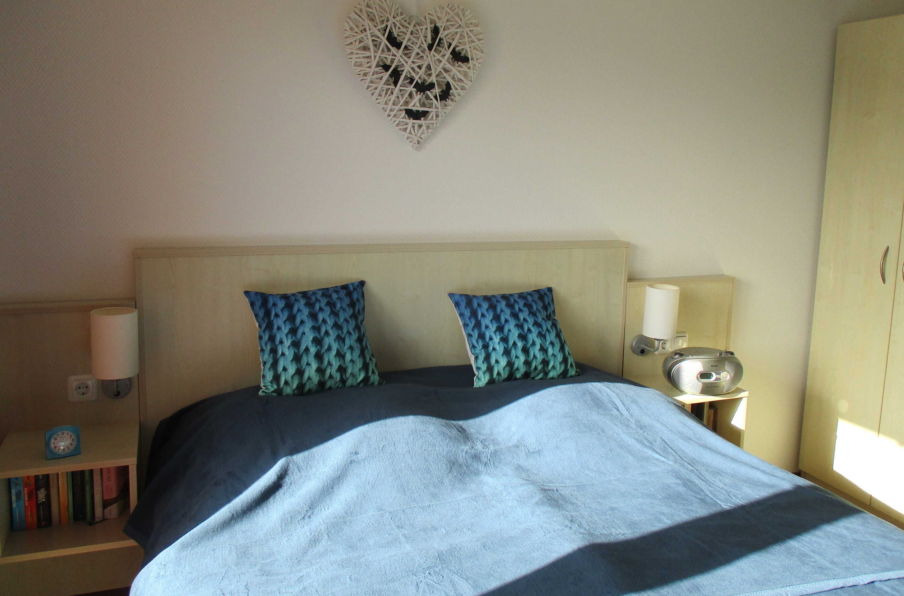 A bedroom with a bed, two patterned pillows, a bedside lamp, a clock, and a wall decoration.