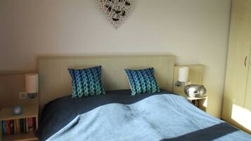 A bedroom with a bed, two patterned pillows, a bedside lamp, a clock, and a wall decoration.