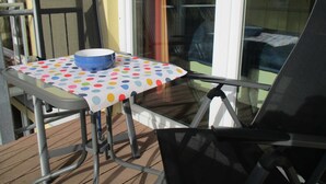 Een terras met een tafel, bedekt met een tafelkleed met stippen, een blauwe kom en twee stoelen.