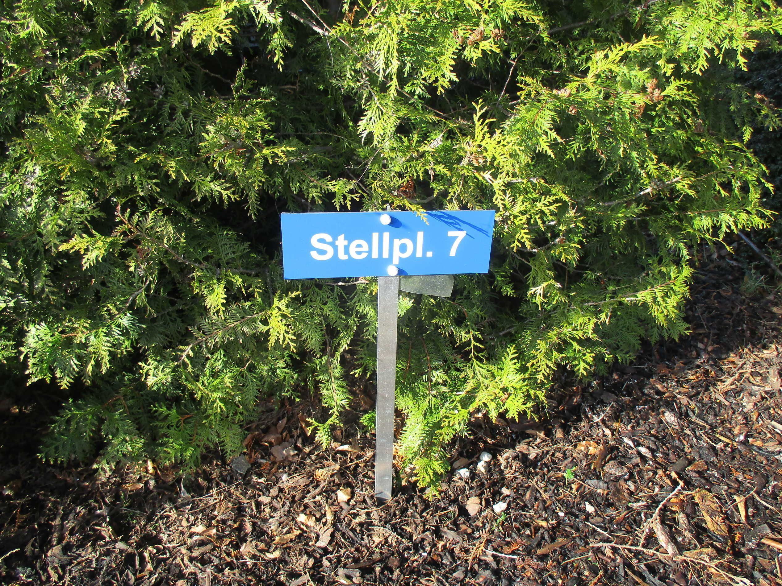 A street sign reading "Stellpl. 7" in front of dense green foliage.