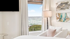 Un dormitorio con un ventanal grande que ofrece vistas al océano, un televisor de pantalla plana montado en la pared y obras de arte decorando la pared.