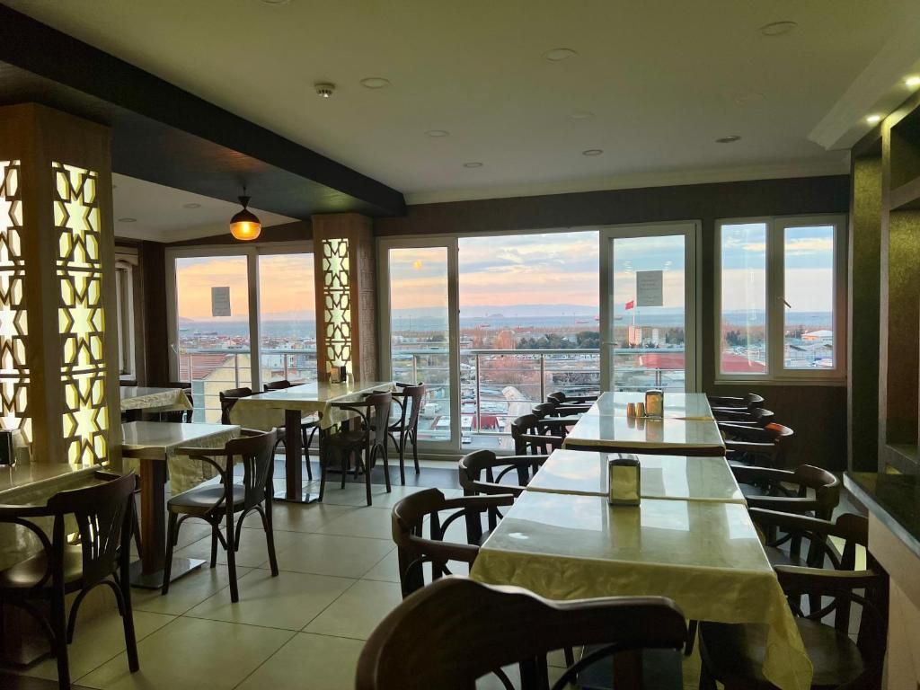 Un restaurante con una mesa larga y sillas, ventanas amplias con vista a la ciudad y paneles decorativos en la pared.
