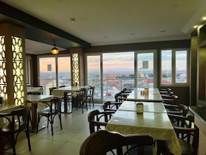 A restaurant with a long table and chairs, large windows with a view of the city, and decorative wall panels. - Elit Palace Hotel (Istanbul)