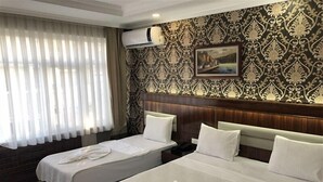 Habitación de hotel con dos camas, un ventanal con cortinas translúcidas, un equipo de aire acondicionado y un papel tapiz estampado.