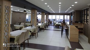 Un restaurante espacioso con numerosas mesas y sillas, ventanas amplias que ofrecen vistas y un diseño de techo moderno con iluminación empotrada.