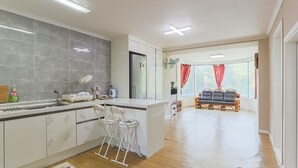 Een ruime keuken met een centraal eiland, een zithoek met een bank en stoelen, en uitzicht op de omgeving door grote ramen.