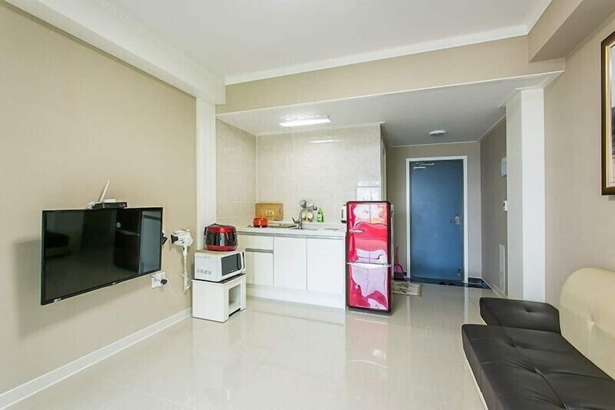 Un espacio habitable pequeño con kitchenette, un televisor de pantalla plana en la pared, un refrigerador y un sofá.