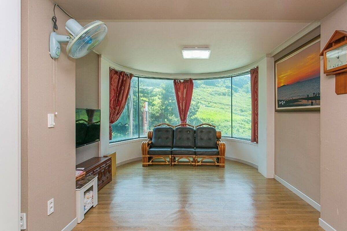 Una habitación amplia con techo curvo, un ventanal con cortinas, un banco de madera, un reloj colgado en la pared y un ventilador de techo.