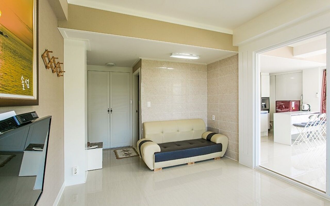 A modern living room with a sofa, a piano, and a sliding glass door leading to a kitchen area.