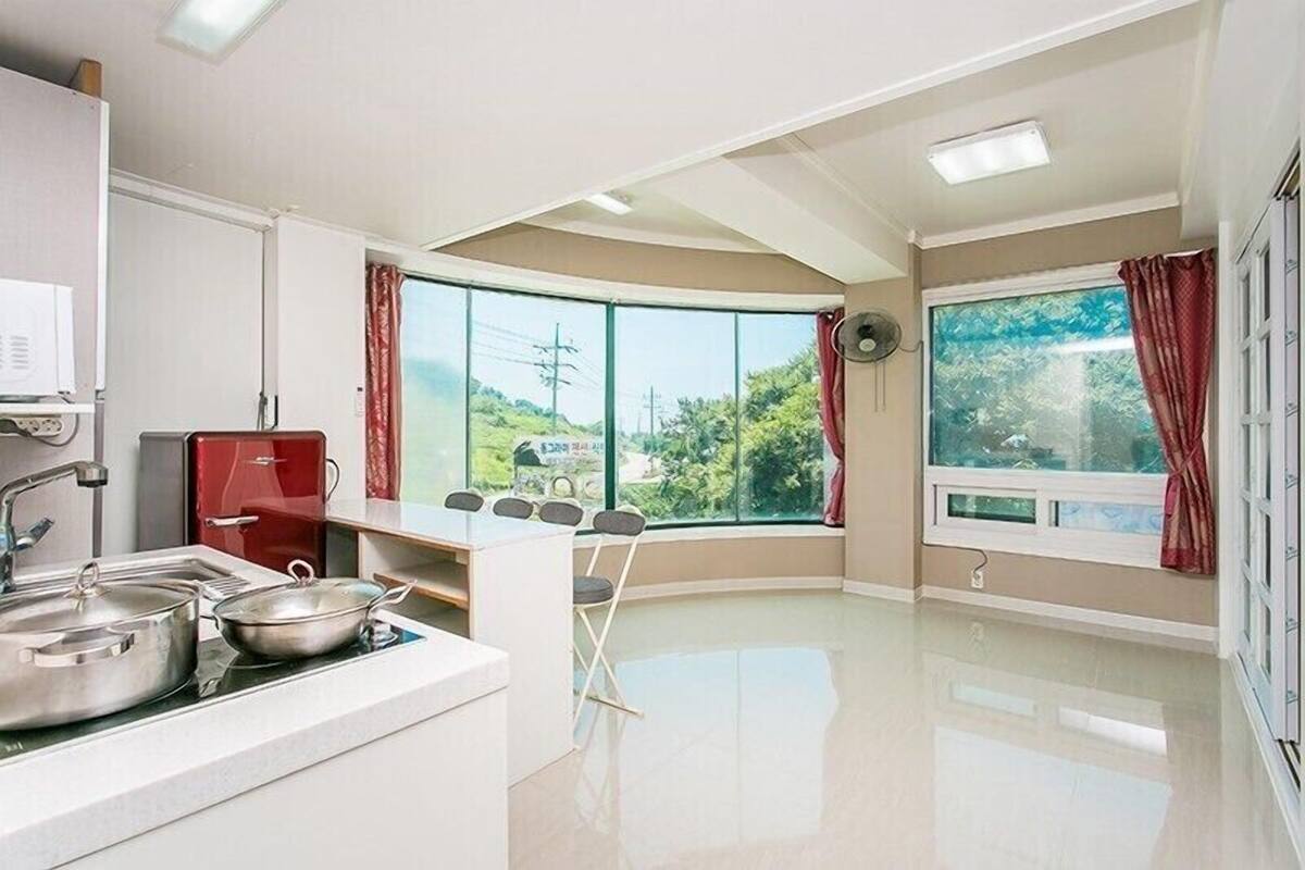Una cocina con un ventanal grande, microondas, un armario rojo y un comedor con sillas.