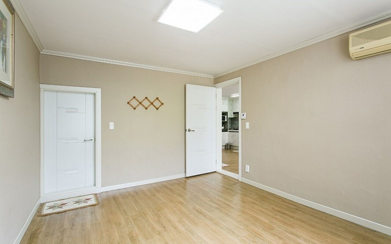 A spacious room with hardwood flooring, two white doors, a ceiling light, and a wall-mounted air conditioning unit.