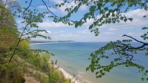 Un paysage côtier avec une plage, un ciel dégagé et des reliefs visibles au loin.