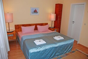 Une chambre d’hôtel avec un lit double, deux tables de chevet, une commode, une porte et un tableau encadré au mur.