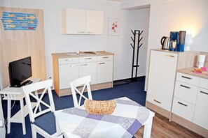 Una habitación de hotel compacta con kitchenette, un comedor con mesa y sillas, un televisor y una cama.