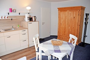 A compact kitchen with a sink, coffee maker, and cabinets. There is a dining table with chairs and a wooden cabinet.