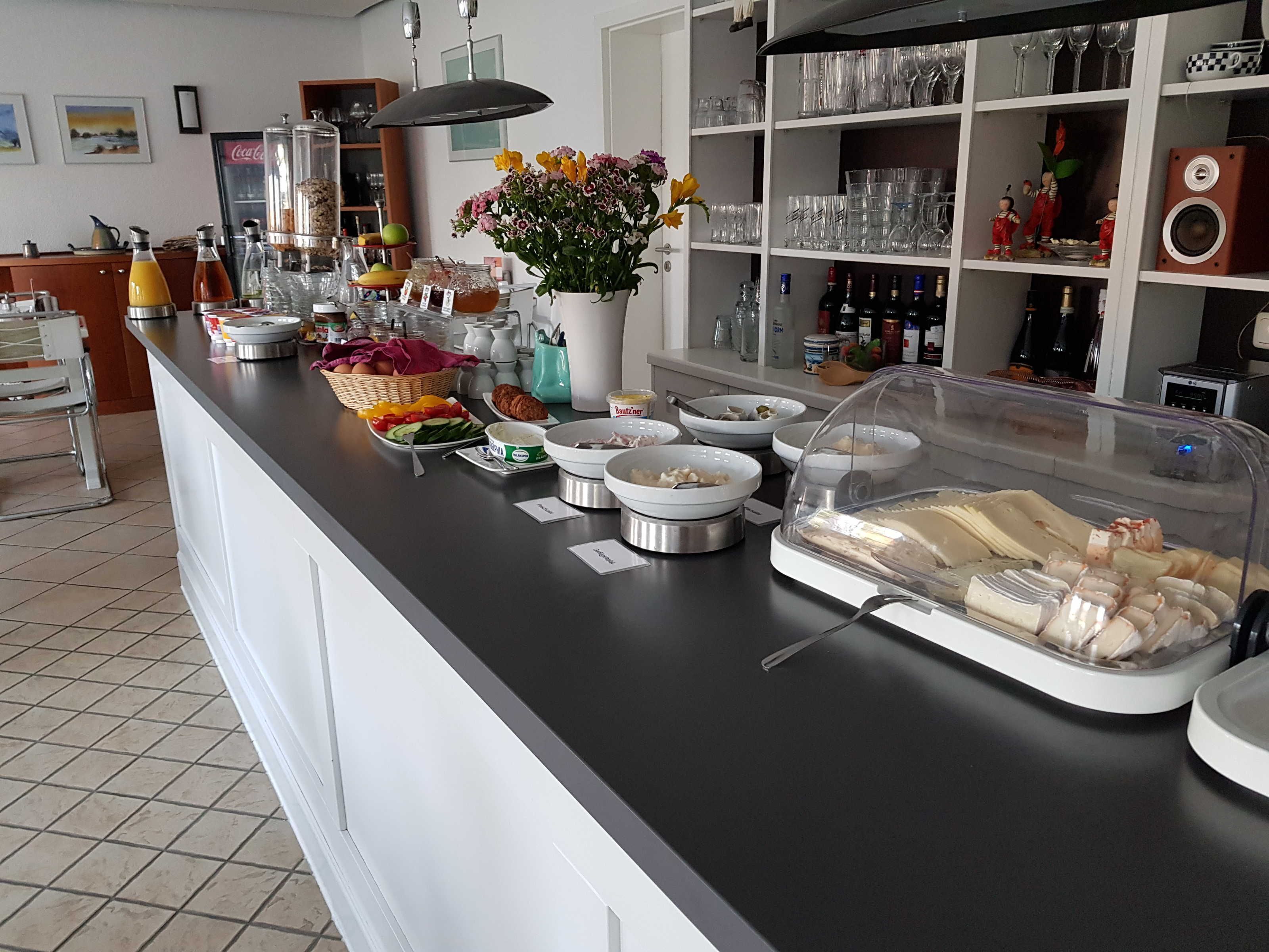 A buffet setup with various food items, a flower arrangement, and a wine and glass display.