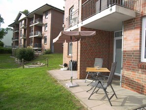 A brick building with a balcony, a small garden area, and outdoor seating.