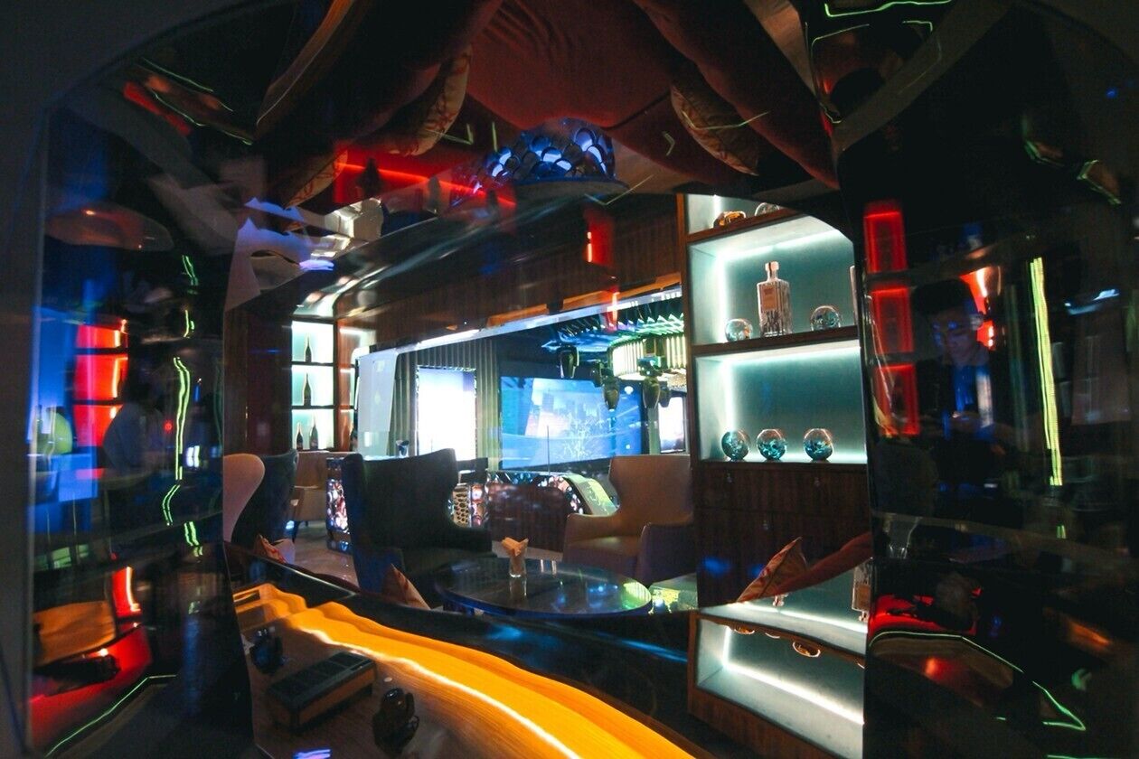 A modern bar area with a glass partition, bar stools, and shelves with bottles.