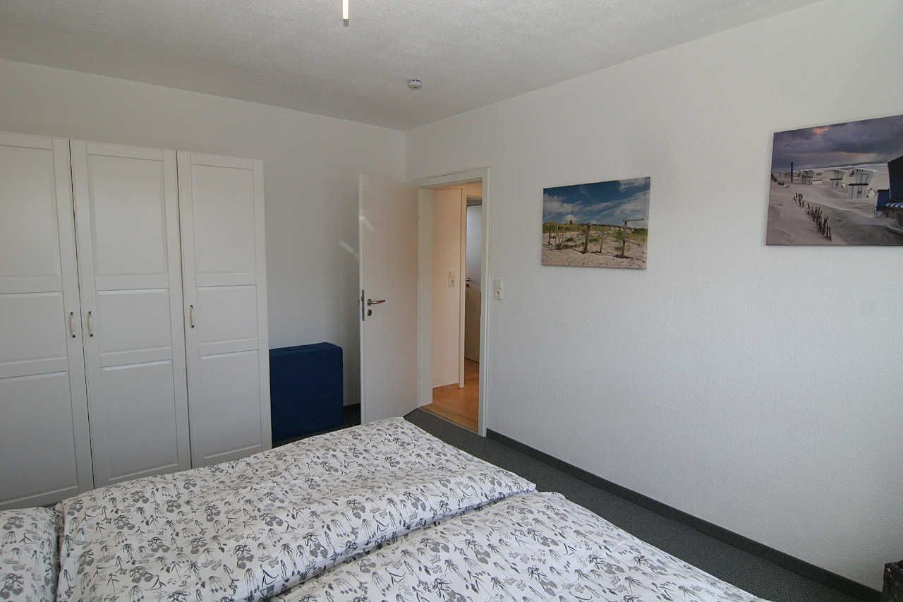 A bedroom with two beds, a wardrobe, and a door leading to another room.